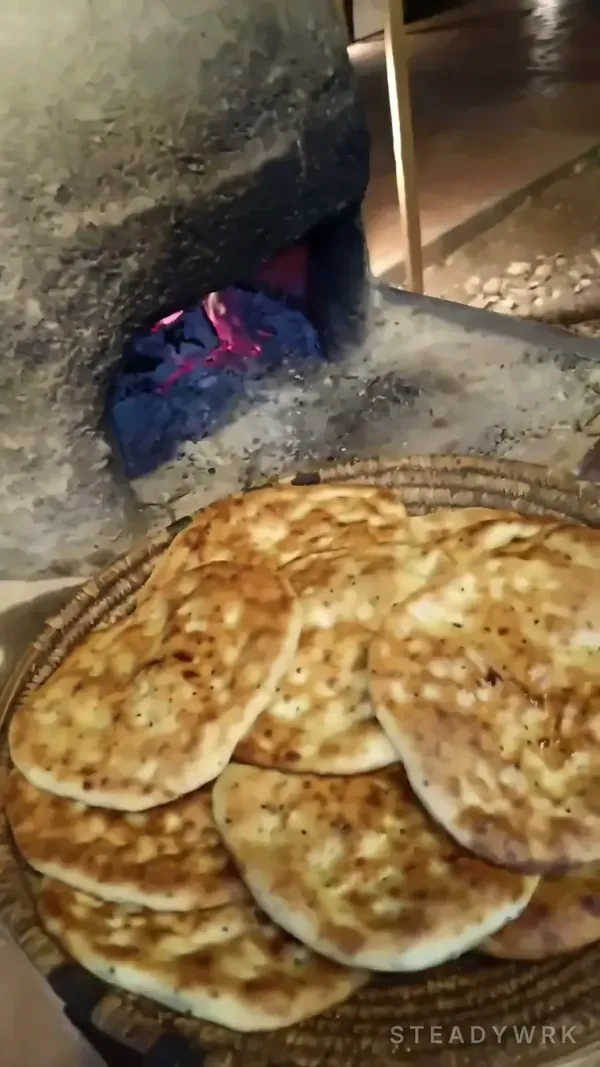 Fresh taboun bread on a straw tray in front of the glowing oven
